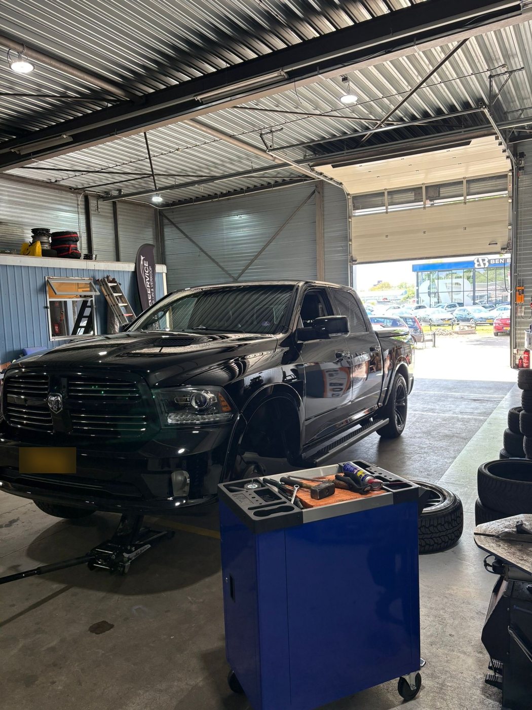 Zwarte Dodge Ram pick-up op de brug in de werkplaats, met een gereedschapswagen op de voorgrond