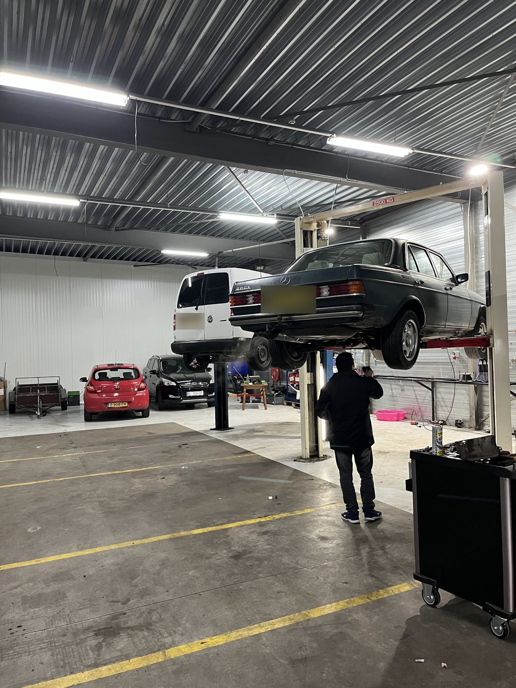 Een klassieke Mercedes op de brug in de werkplaats van A.B.Autoservice, met een monteur eronder