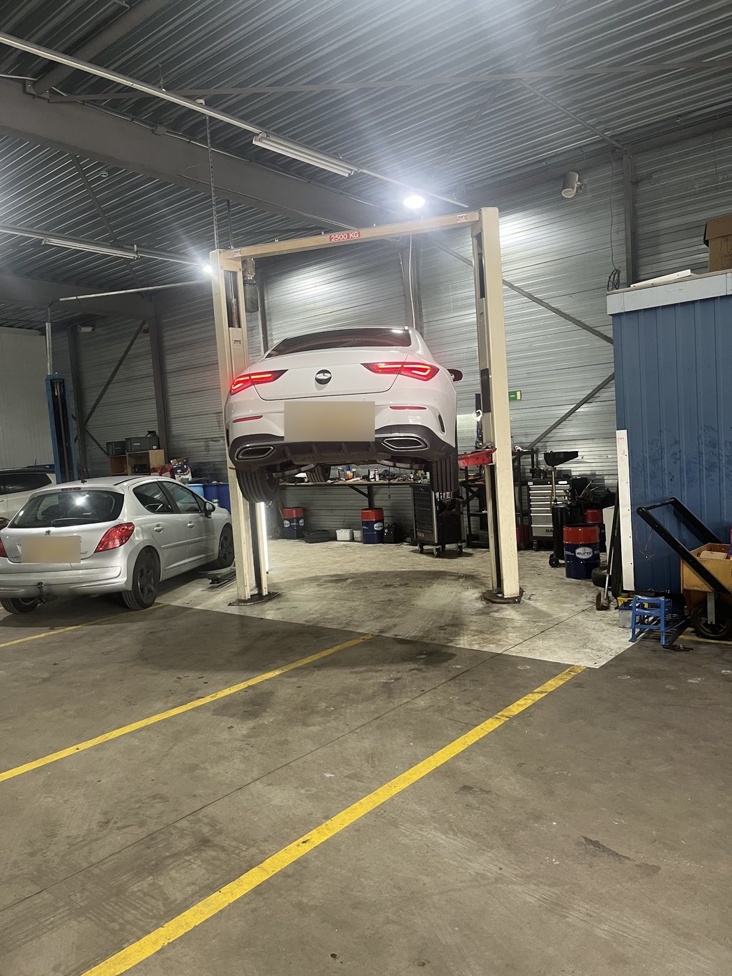 Witte Mercedes op de tweekolomsbrug, met andere auto's van klanten in de werkplaats